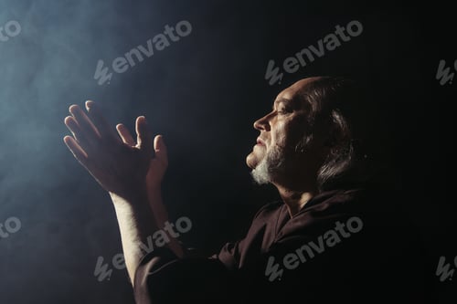Preview: side view of medieval priest praying on black background with smoke