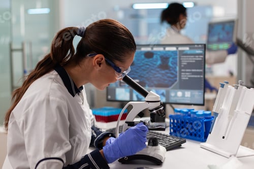 Preview: Scientist with protection glasses researching sample looking through microscope