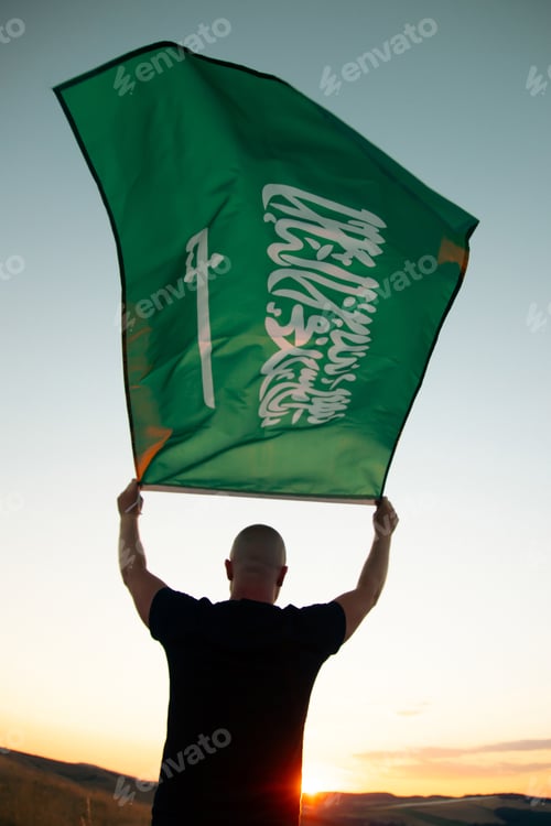 Preview: Man holding Saudi Arabia national flag waving in beautiful clouds.