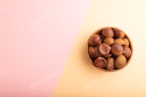 Preview: wooden bowl with raw edible Сhestnuts on pink and orange paper top view, flat lay, copy space