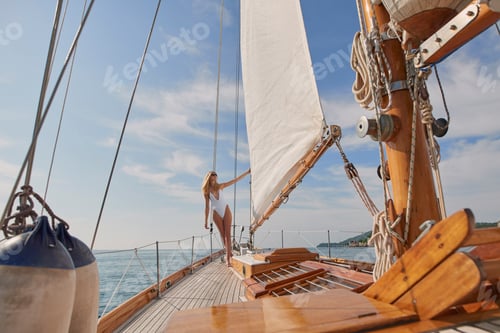 Preview: Blonde woman in white swimsuit holding yachts sail enjoying the sun. Young woman in white swimsuit
