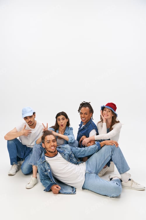 Preview: cheerful woman showing horns gesture near trendy african american man lying down on grey backdrop