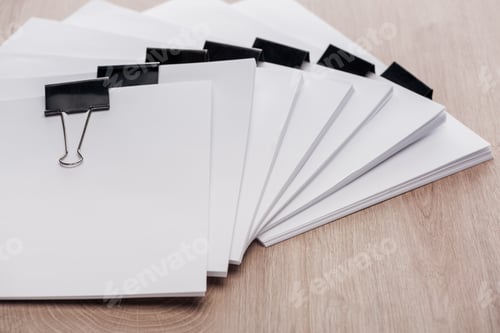 Preview: stacks of blank paper with metal binder clips and copy space on wooden desk