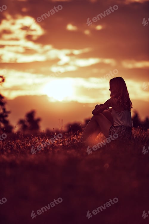Preview: Silhouette Of A Woman Sitting On A Field.