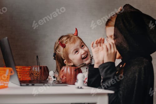 Preview: Online Halloween celebration. Happy kids in costumes having video call, using notebook, having fun