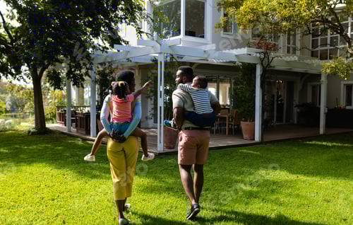 Preview: Rear view of african american mother and daughter piggybacking children in yard outside house