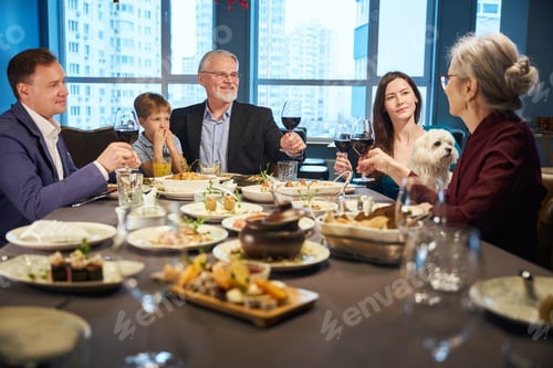 Preview: Family enjoy Christmas dinner together in restaurant raising glasses with wine