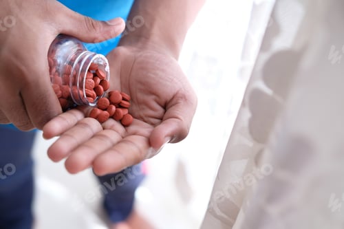 Preview: In one hand, there is a container of medication, and the other hand is held out