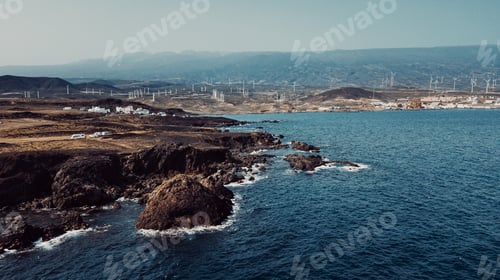 Preview: Aerial coast view of rocks and ocean waves with little town in background. Blue sky and ocean