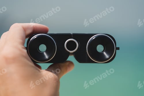 Preview: Hand holding retro binoculars at the beach
