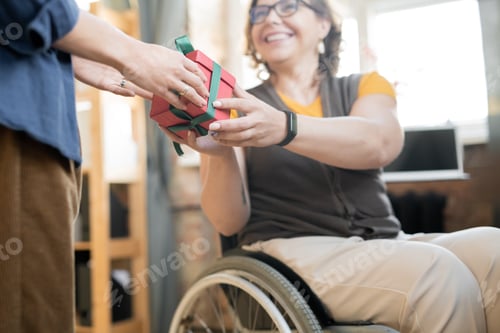 Preview: Young cheerful disable businesswoman passing giftbox with present to colleague