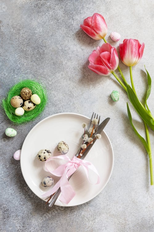 Preview: Festive Easter table setting with painted eggs, spring flowers and cutlery on light grey tabletop.