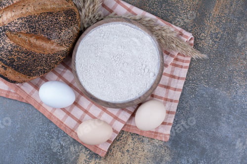 Preview: Eggs, bowl of flour and sesame coated bread on a towel on marble background
