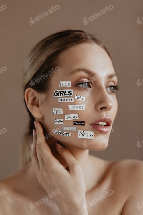 Preview: Beautiful woman with words-stickers on her face looks into distance on beige background