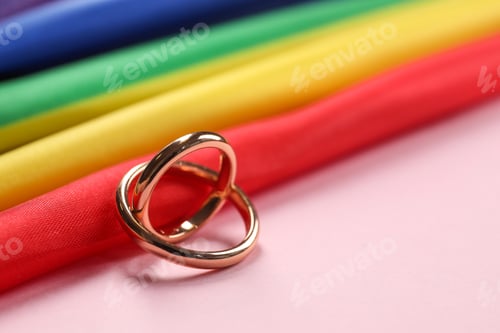 Preview: Rainbow LGBT flag and wedding rings on pink background, closeup