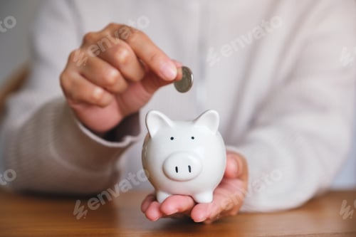 Preview: Closeup image of a woman putting coins into piggy bank for saving money concept