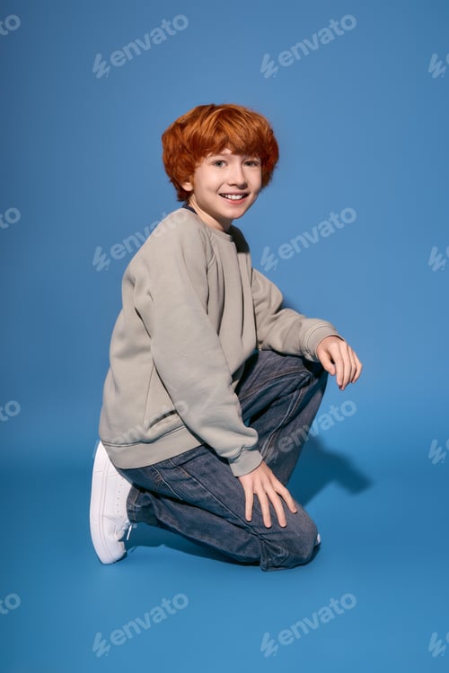 Preview: Stylish boy with curly red hair strikes a playful pose against a vibrant blue backdrop