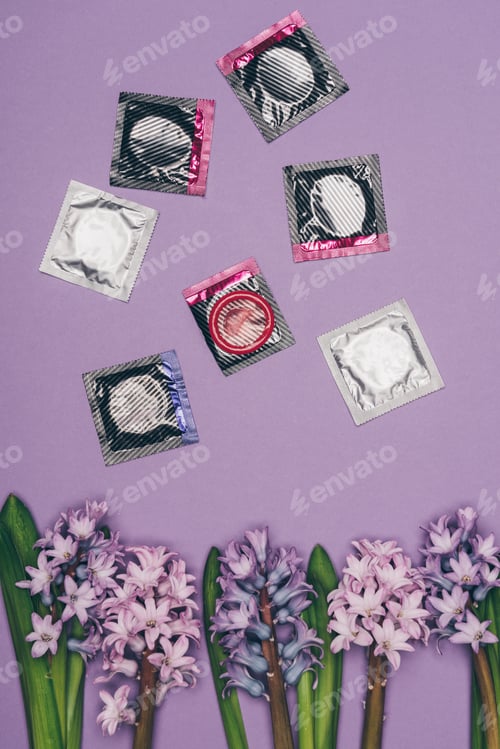 Preview: top view of condoms and arranged flowers isolated on purple