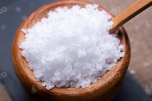 Preview: Closeup of a wooden bowl full of sea salt on a black stone board