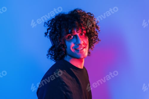 Preview: Young beautiful man with curly hair is indoors in the studio with neon lighting