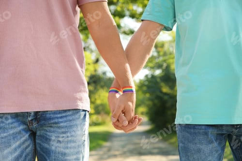 Preview: Gay couple with wristbands holding hands outdoors, closeup