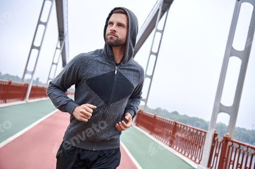 Preview: Morning workout. Close up of young man in sports clothing exercising while jogging on the bridge
