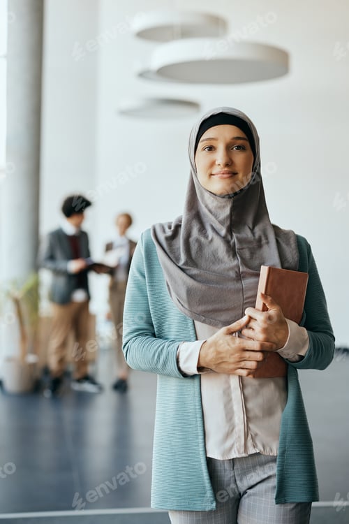 Preview: Middle Eastern businesswoman standing in hallway of an office building and looking at camera.