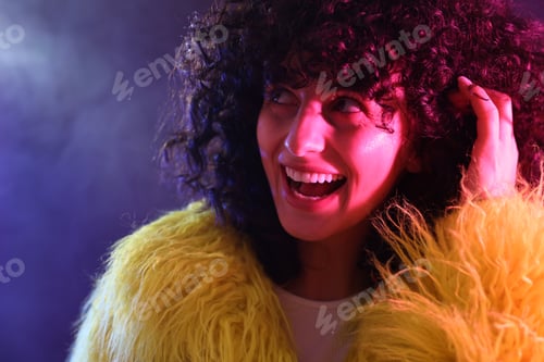 Preview: Beautiful young woman in yellow fur coat on color background in neon lights, closeup