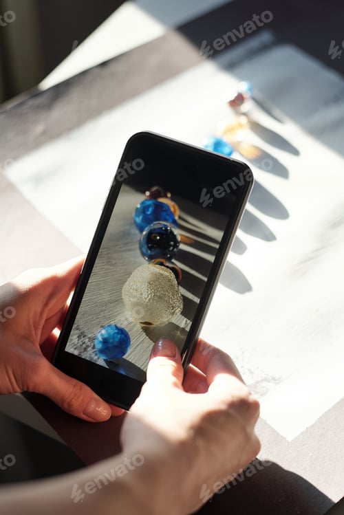 Preview: Hands of young female with smartphone taking photo of row of large glass beads