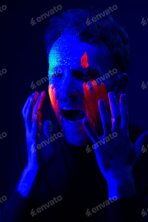 Preview: Fashion portrait. A man with fluorescent paint on his face under neon light.