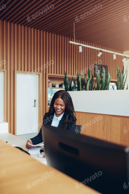 Preview: Smiling African American businesswoman sorting paperwork at a reception desk