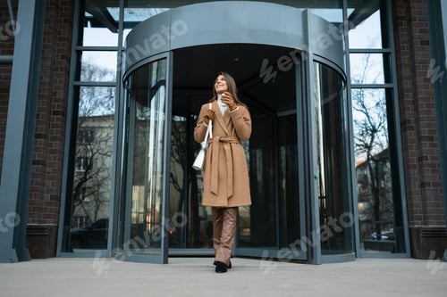 Preview: Smiling girl walking out of office building with a cup of coffee in hand