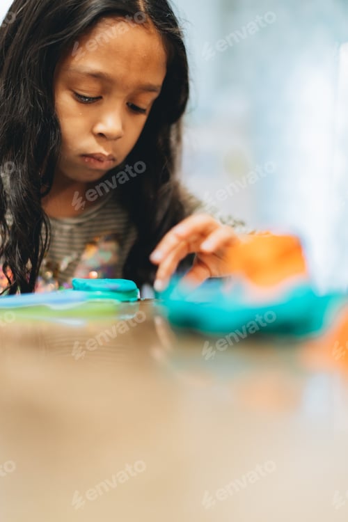Preview: Diverse mixed race pre school age girl at home playing with modeling clay having fun learning