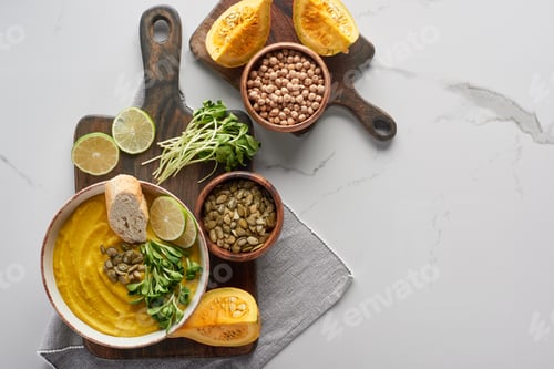 Preview: top view of tasty mashed pumpkin soup on wooden cutting board with ingredients on marble surface