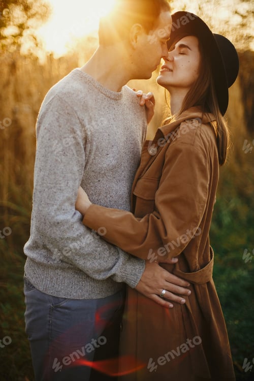 Preview: Happy stylish couple embracing in autumn meadow in warm sunset light