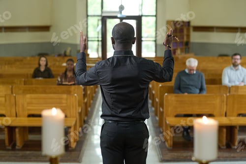 Preview: Back of African American priest in black shirt and pants blessing parishioners