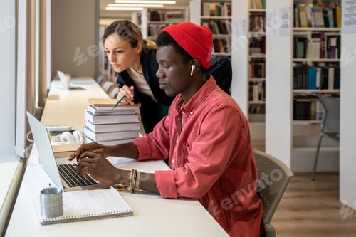 Preview: Interested african american student typing on laptop near focused college teacher looking at screen