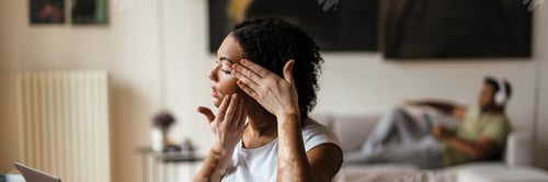 Preview: Woman with vitiligo massaging face while working with laptop at home