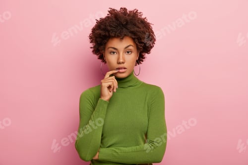 Vista previa: Horizontal shot of serious calm dark skinned curly woman wears round earrings, green turtleneck, kee
