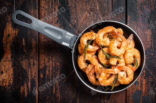 Preview: Fried with butter and garlic prawns shrimps in a skillet. Wooden background. Top view