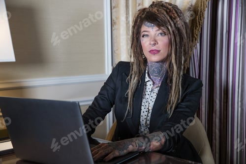 Preview: Pretty woman with tattoos and dreadlocks typing on computer