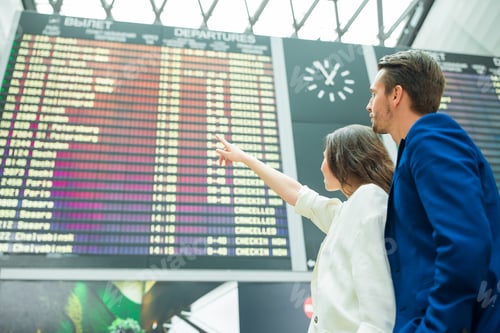 Preview: Young couple in international airport looking at the flight information board