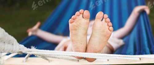 Preview: closeup of little girl's feet relaxing in the blue hammock during her summer vacation in back yard