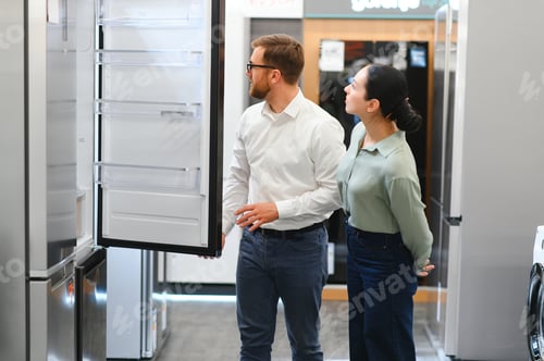 Preview: shop assistant demonstrates refrigerator to young woman in home appliance shopping mall supermarket