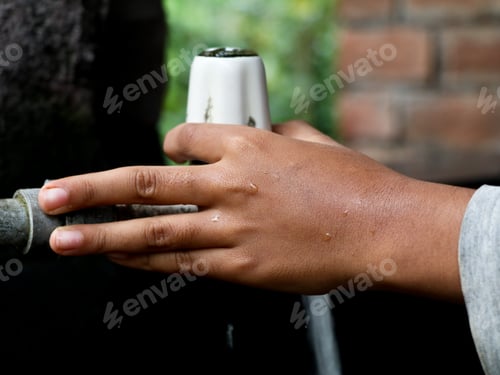 Preview: Hand of a boy turning on an old plastic water tap
