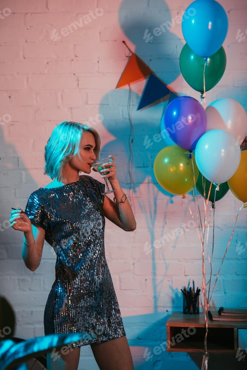 Preview: Blonde woman drinking cocktail at party by colorful balloons