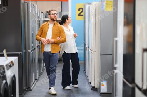 Preview: Young couple, satisfied customers choosing fridge in appliances store