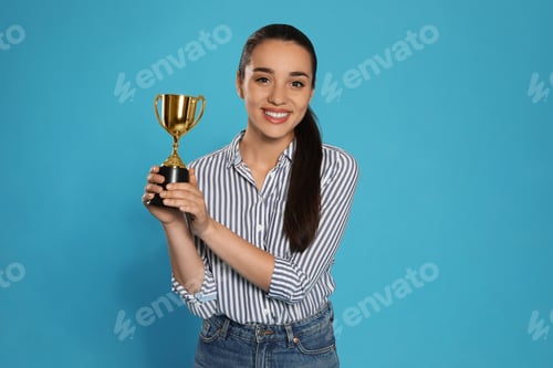 Preview: Portrait of happy young woman with gold trophy cup on blue background