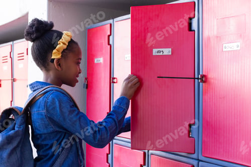 Preview: Opening locker, african american girl with backpack organizing school supplies in hallway
