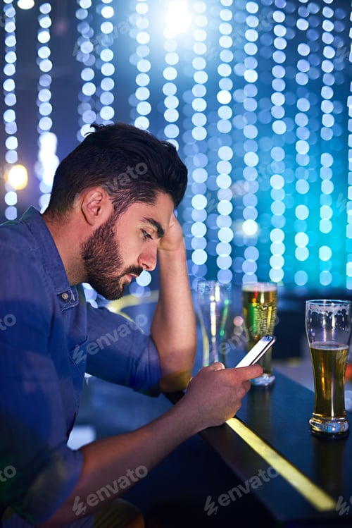 Preview: Shot of a young man looking upset while using his phone at a bar